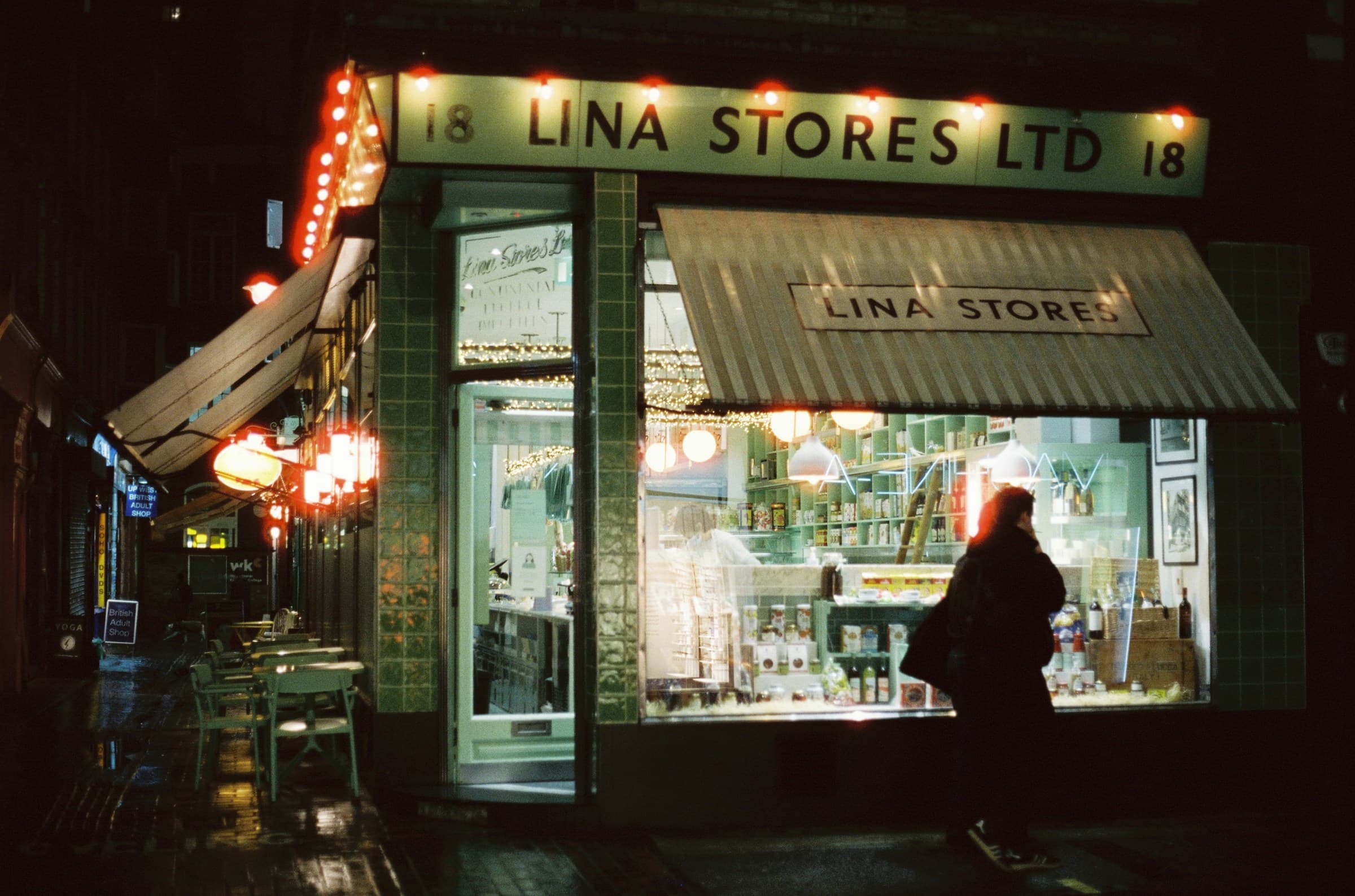 A passerby outside a warmly lit neighbourhood storefront at night